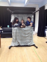 Three actors testing the upright bed. Sheets parted in the center to allow a third actor to appear during the scene.